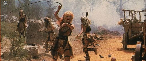 Amazon warrior woman from the future wields a whip, while other female members of her society run in the background.